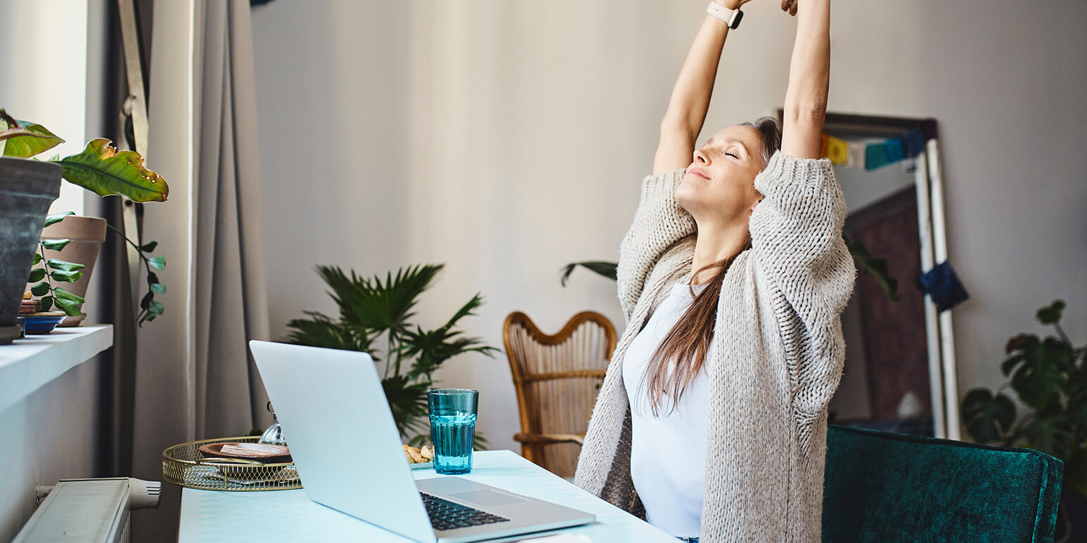 Freelancer with eyes closed stretching arms sitting at desk