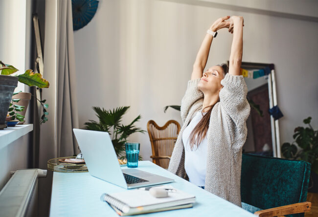 Freelancer with eyes closed stretching arms sitting at desk