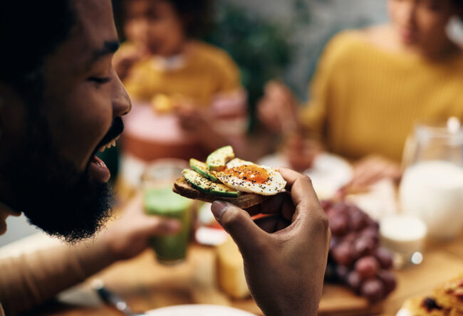 Close-up of black man eating healthy sandwich at home.