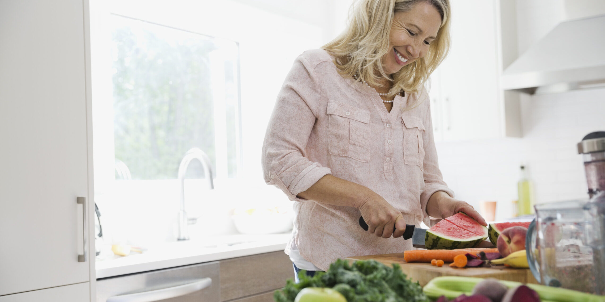 Happy woman cutting watermelon at kitchen counter