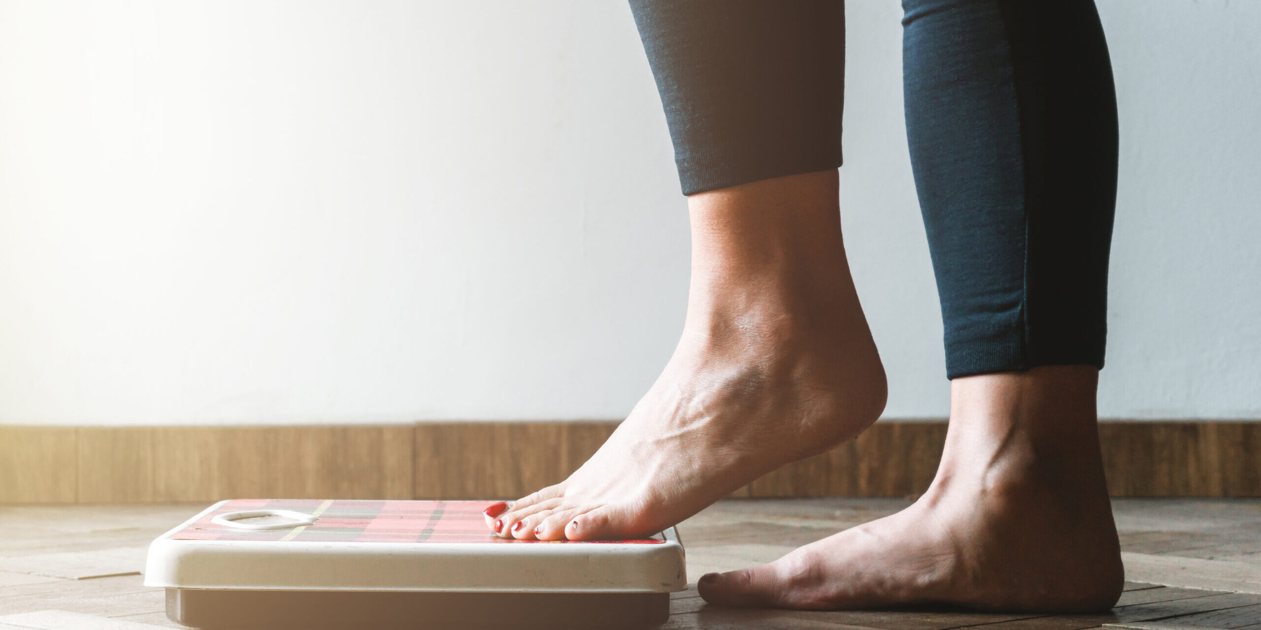 Female checking kilogrammes getting on the scale – self care and body positivity concept – warm flare on left