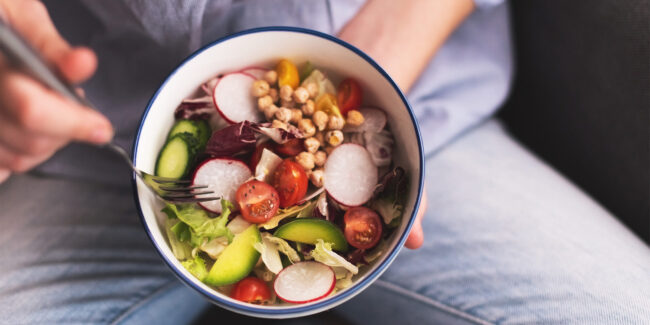 Green vegan breakfast meal in bowl with spinach, arugula, avocado, seeds and sprouts. Girl in leggins holding plate with hands visible, top view. Clean eating, dieting, vegan food concept