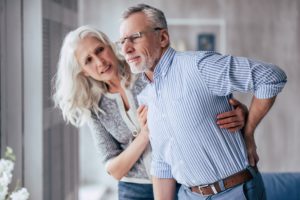 Man experiencing back pain, woman helping him to stand up