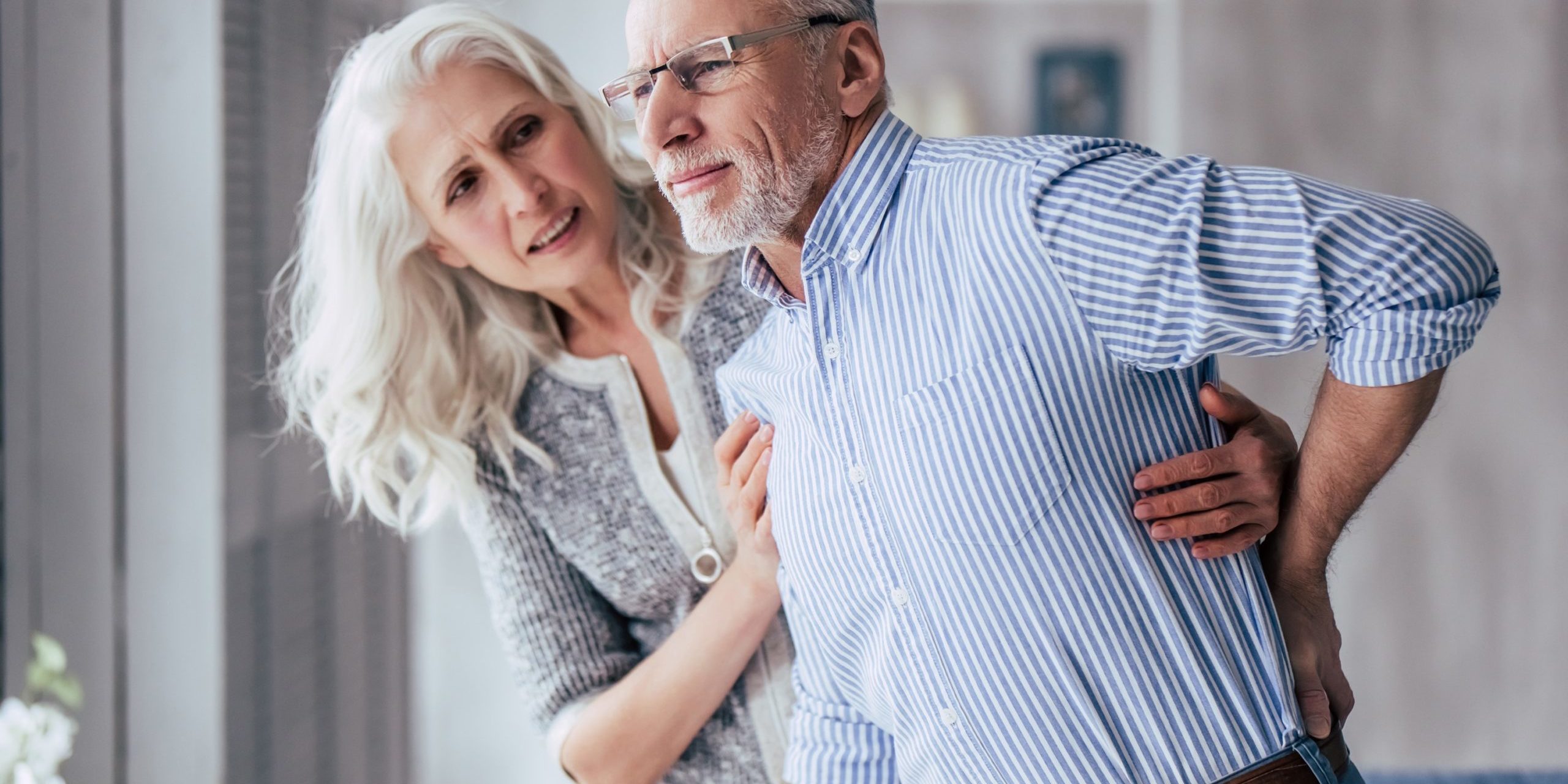 Back pain couple Man experiencing back pain, woman helping him to stand up