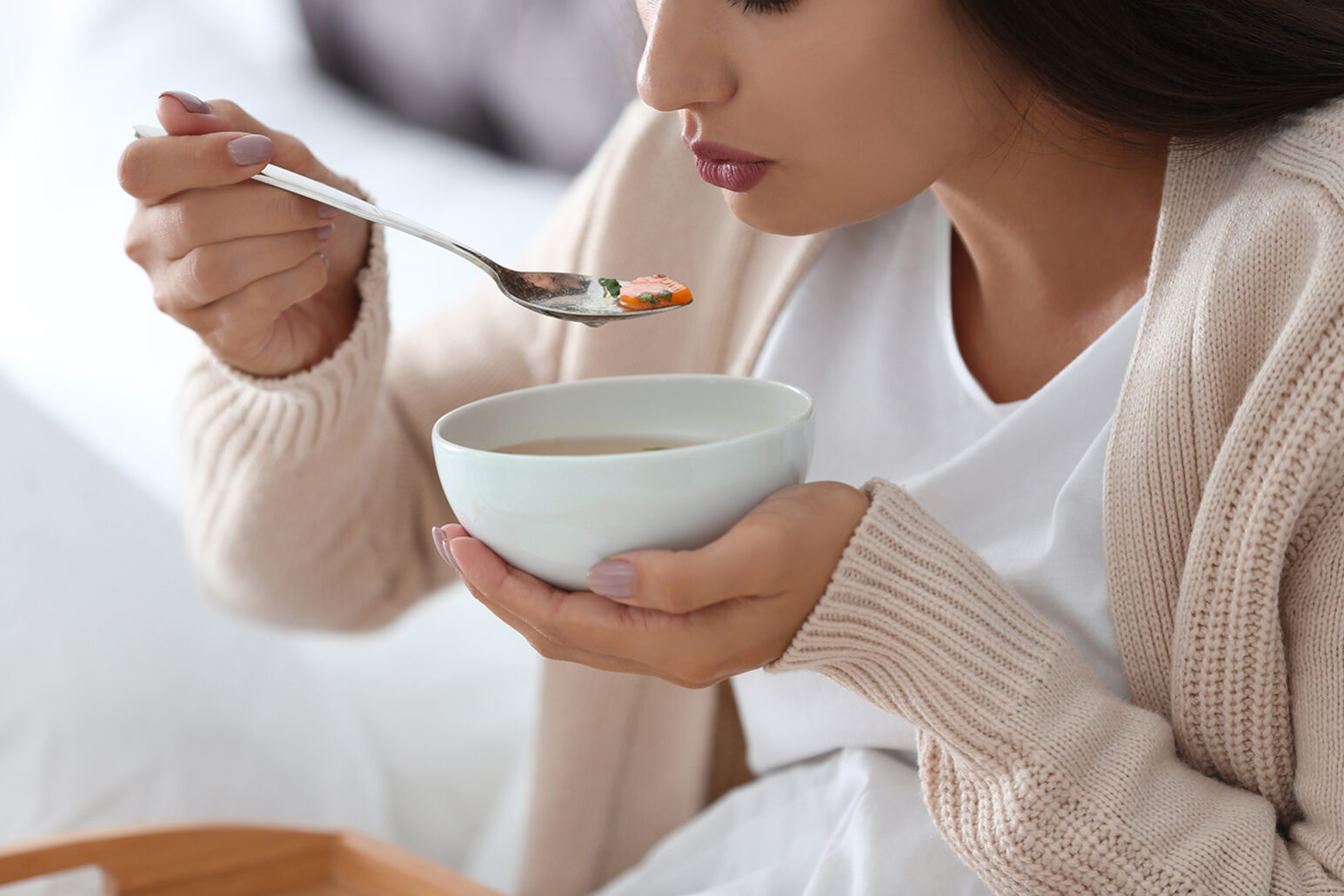 Sick young woman eating soup to cure flu at home