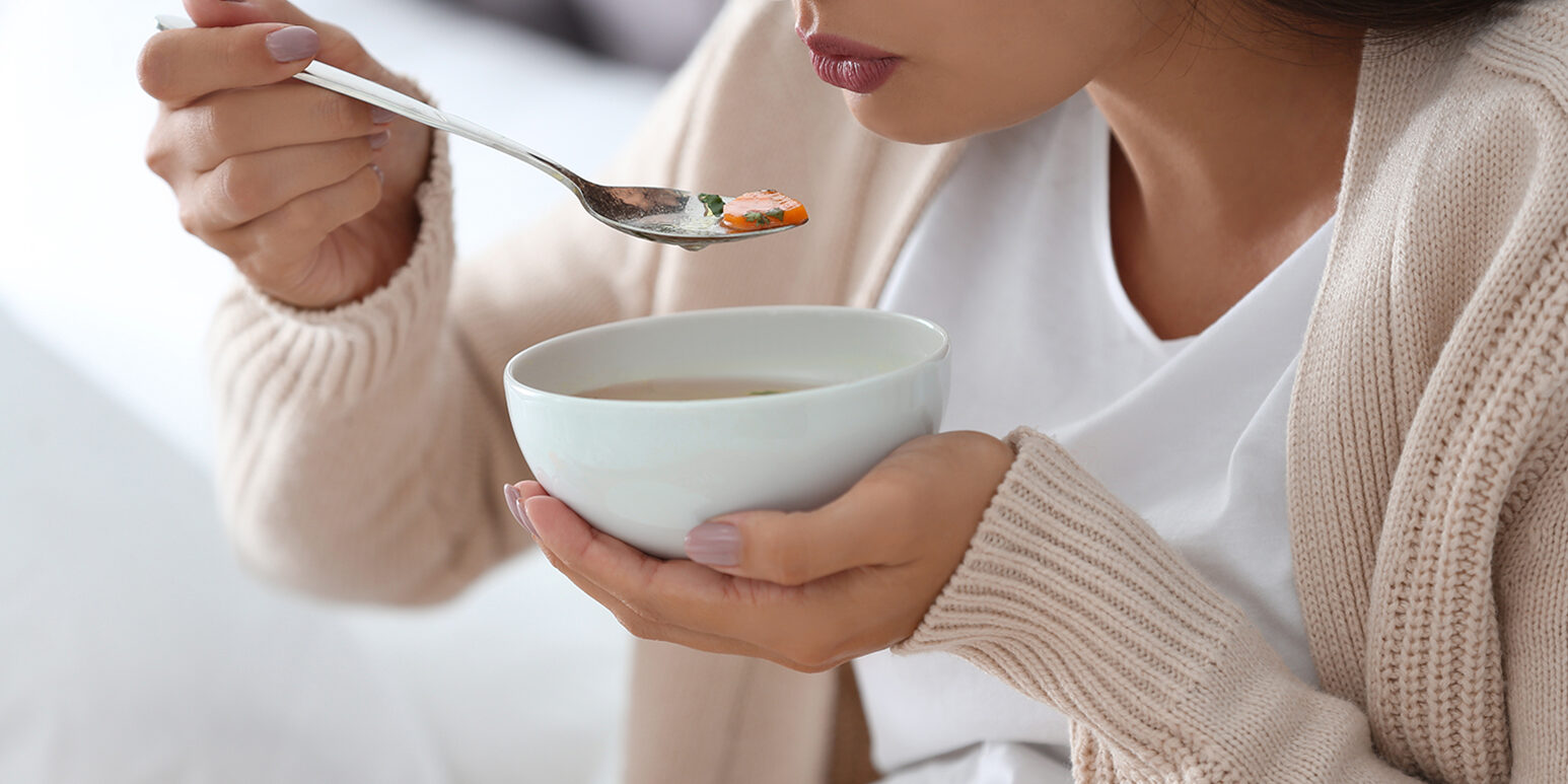 Sick young woman eating soup to cure flu at home