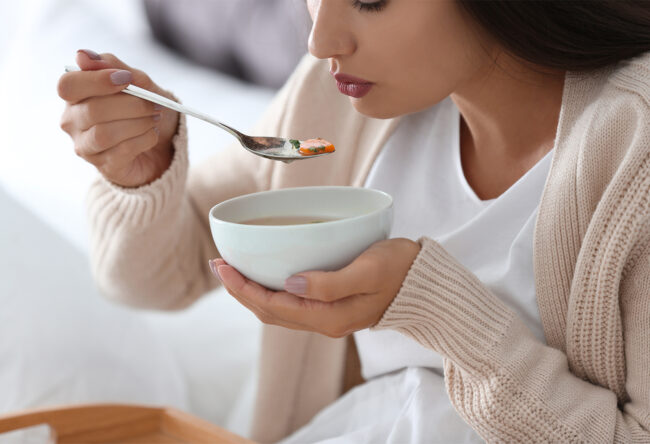 Sick young woman eating soup to cure flu at home