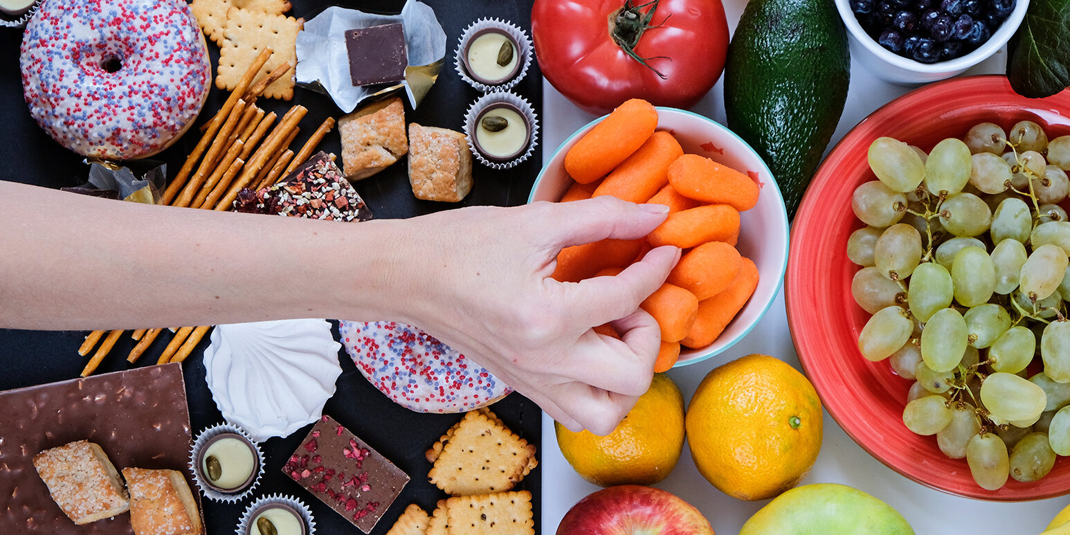 Healthy and unhealthy food concept, fruits and vegetables vs donuts, sweets and chocolate with woman’s hand. Top view