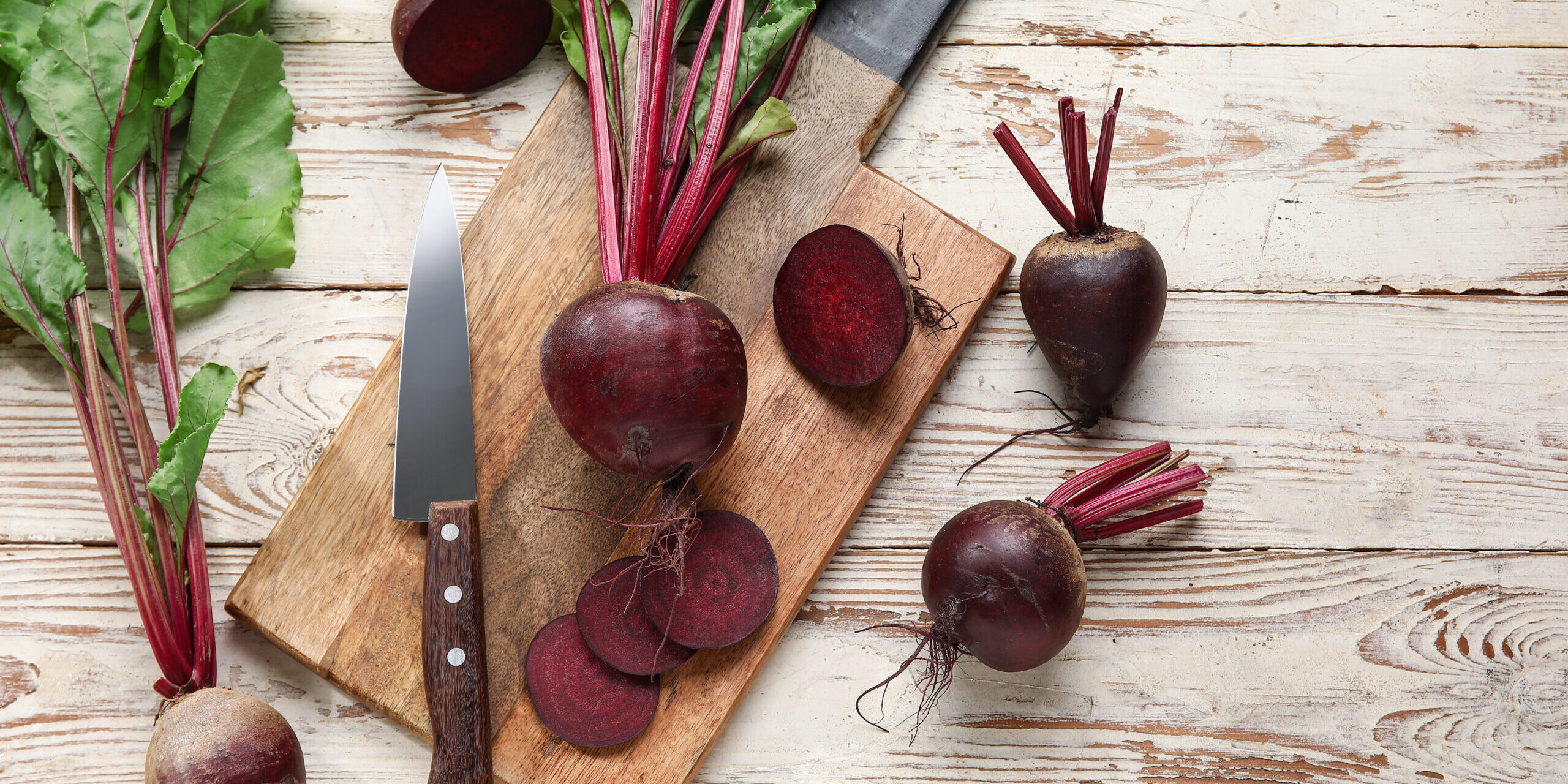 Board of fresh beets with green leaves on wooden background