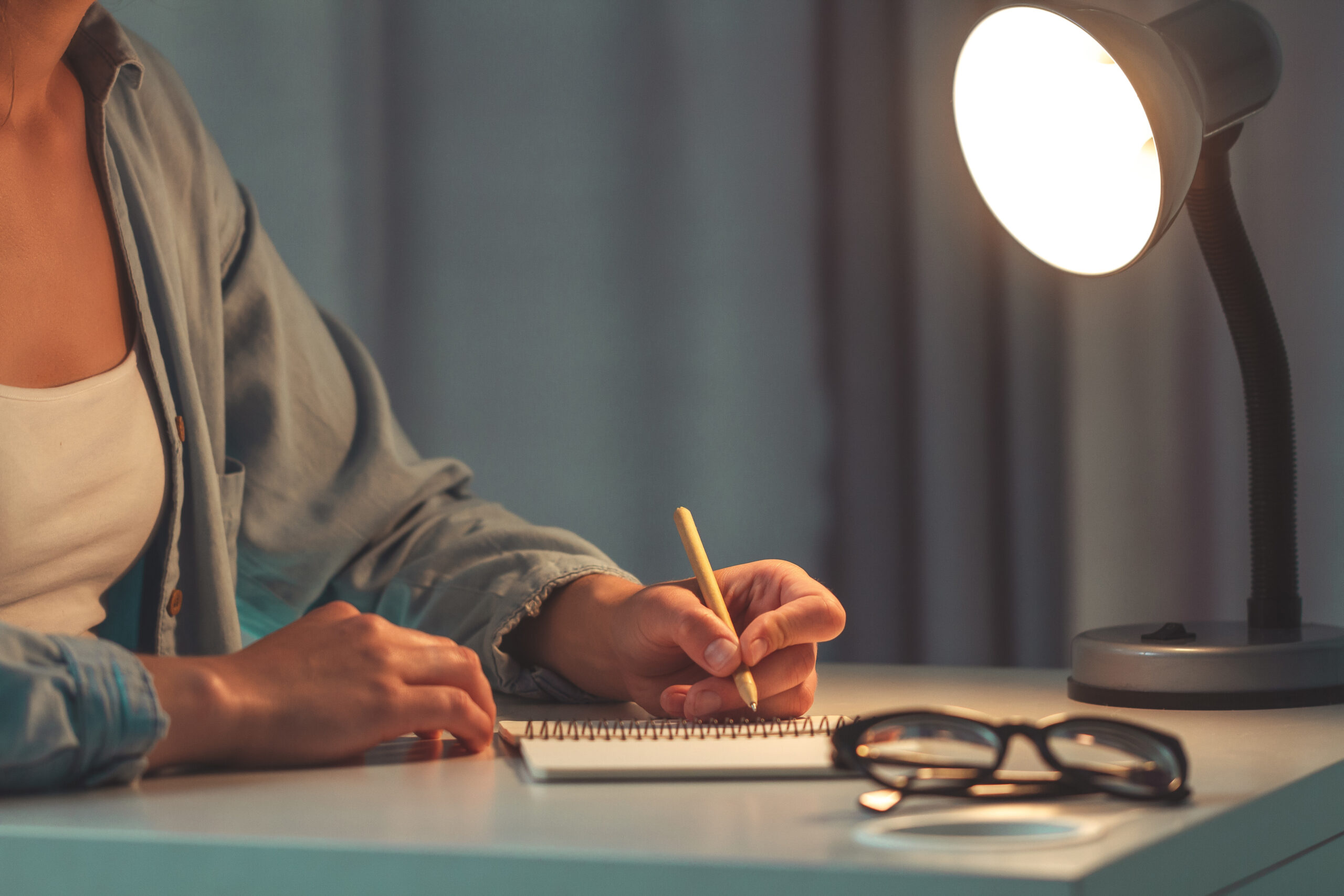 Female with eco pen writing something on paper and working using notebook. Woman write thoughts in a diary at the evening at home.